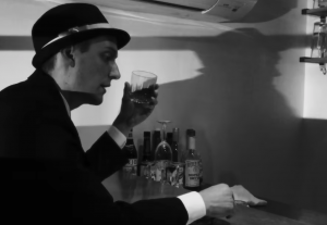 A screenshot from All Our Sins Remembered, showing a man in a fedora holding a drink, sitting at a bar